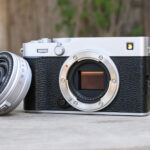 Fujifilm X-E5 on a wooden bench, with the XF 23mm f/2.8 lens removed and propped up against the camera