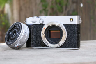 Fujifilm X-E5 on a wooden bench, with the XF 23mm f/2.8 lens removed and propped up against the camera