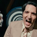 David Dastmalchian laughs maniacally in front of a hypnotic background in Late Night with the Devil