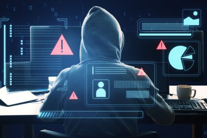 A hacker wearing a hoodie sitting at a computer, his face hidden.