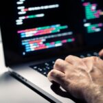 Hacker with malware code in computer screen. Cybersecurity, privacy or cyber attack. Programmer or fraud criminal writing virus software. Online firewall and privacy crime. Web data engineer