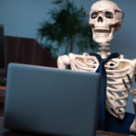 Skeleton of an office worker waiting for their laptop to boot