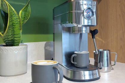 Casabrews 5418 Pro coffee maker on kitchen counter with coffee cups, milk pitcher, and plant