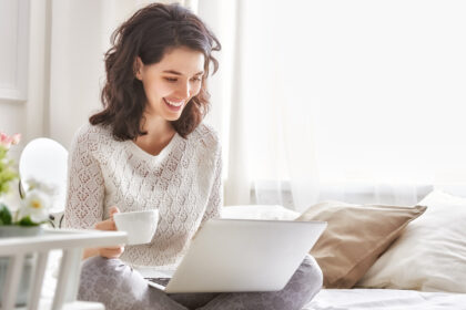 Happy woman sitting on a bed with a coffee and a Windows 10 laptop