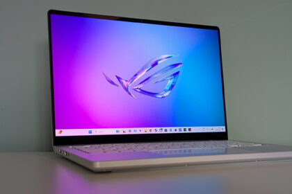 Three-quarter view of Asus ROG Zephyrus G14 (2025) open on desk with green wall in background