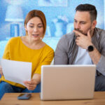 Couple looking at bills whilst sitting on a sofa, in front of a laptop