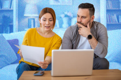 Couple looking at bills whilst sitting on a sofa, in front of a laptop