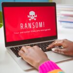 A laptop with a red screen with a white skull on it with the message: &quot;RANSOMWARE. All your files are encrypted.&quot;