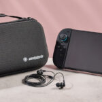 The Nintendo Switch 2 sitting side-by-side with the Snakebyte Starter Kit S2 case; in between them sits the Snakebyte wired earbuds.