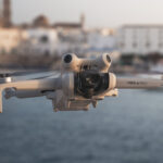 DJI Mini 4 Pro in flight at golden hour with ocean and seaside town in the background
