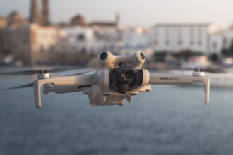 DJI Mini 4 Pro in flight at golden hour with ocean and seaside town in the background