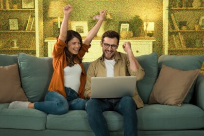 Young couple looking excited whilst sitting on sofa with a laptop.