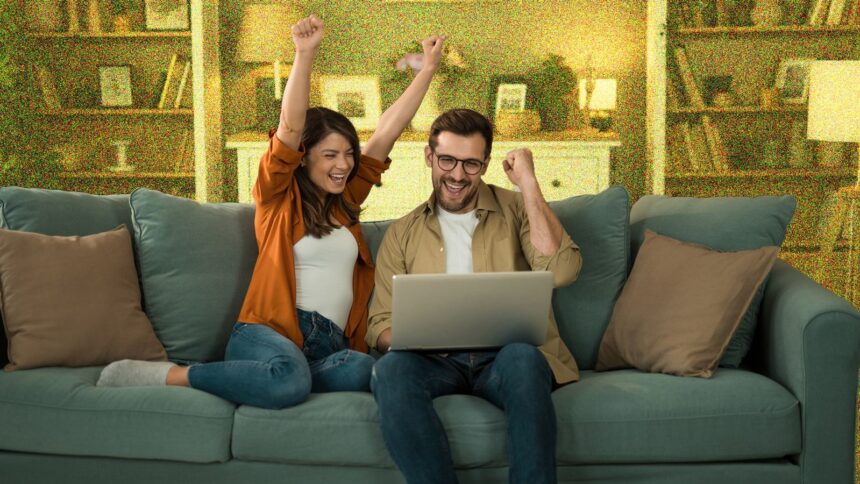 Young couple looking excited whilst sitting on sofa with a laptop.