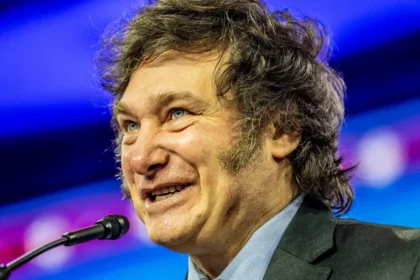 Javier Milei delivering a passionate speech on stage, gesturing emphatically to the audience under bright stage lights.