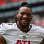 Bijan Robinson smiling at the camera while on the football field during a game.