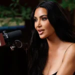 Close-up of Kim Kardashian speaking into a microphone during her Call Her Daddy podcast interview, wearing sleek glam makeup and a neutral-toned outfit.