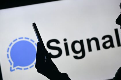 A woman holding a mobile phone in front of the Signal logo displayed on a computer screen