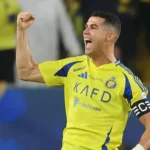 Cristiano Ronaldo celebrating a goal for Al-Nassr, raising his arms in triumph during a Saudi Pro League match.