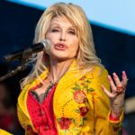 Dolly Parton performs on stage in a bright yellow sequined top during a 2025 concert, radiating her trademark warmth and energy. The country legend, whose net worth is estimated at $650 million, continues to honor the memory of her late husband, Carl Dean, through her music and philanthropy.