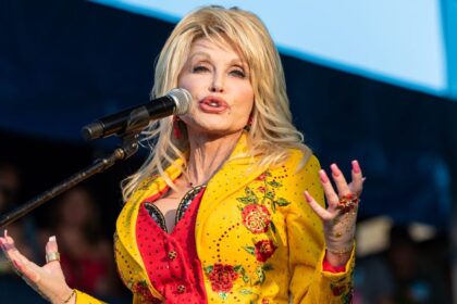 Dolly Parton performs on stage in a bright yellow sequined top during a 2025 concert, radiating her trademark warmth and energy. The country legend, whose net worth is estimated at $650 million, continues to honor the memory of her late husband, Carl Dean, through her music and philanthropy.