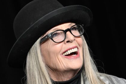 Diane Keaton smiling in signature black hat and glasses during a public appearance in Los Angeles.