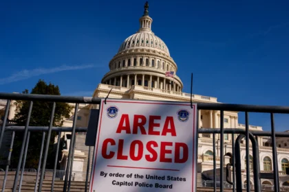 The iconic dome of the United States Capitol building in Washington, D.C., stands before a chain-link fence adorned with a large red "CLOSED" sign, symbolizing the ongoing federal government shutdown.