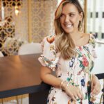 Jewelry designer Kendra Scott posing in a modern kitchen, smiling and dressed casually, highlighting her approachable and creative persona.