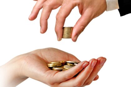 One hand passing coins to another hand, symbolizing wealth transfer.