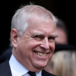 Prince Andrew smiling while attending a recent royal funeral, dressed in formal attire.