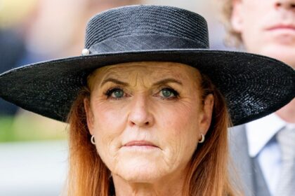 Sarah Ferguson attends a public event wearing a black hat and earrings, appearing thoughtful and composed.