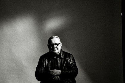 A black and white photo of musician Dave Ball, seated in a recording studio, focusing intently on a mixing console or synthesiser.