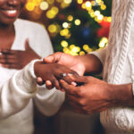 black guy putting diamond ring on girlfriend's finger after proposal