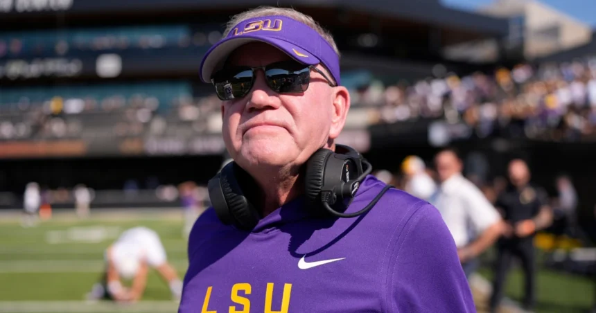 Brian Kelly, LSU Tigers head coach, in purple and gold team gear, wearing headphones and sunglasses during a high-energy practice session.