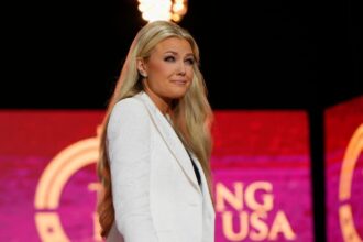 Erika Kirk standing on stage, looking somber and reflective.