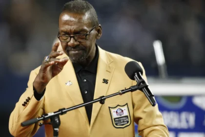 Kenny Easley wearing his Pro Football Hall of Fame gold jacket while speaking at a podium during his enshrinement ceremony.
