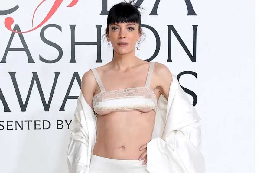 Lily Allen on the red carpet at the CFDA Awards, wearing a sheer, sparkling socking dress and striking a confident pose.