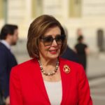 Nancy Pelosi smiling in a red blazer outside the U.S. Capitol building.