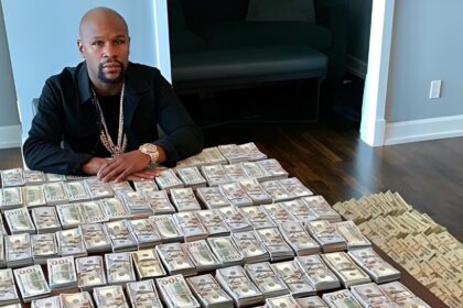 Floyd Mayweather seated at a table covered in stacks of cash, reflecting his long-standing “Money” Mayweather persona.
