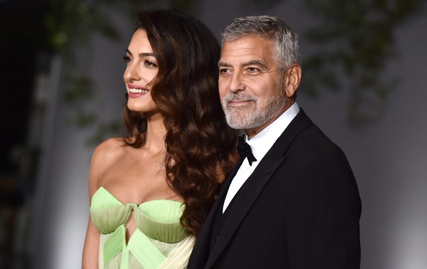 George Clooney and Amal Clooney smiling together on the red carpet at a high-profile event, dressed elegantly and looking happy.